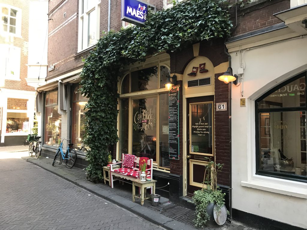 Foto van café de oude mol, een gezellig plekje met groene klimop vboven de deur en gebloemde dekentjes voor de mensen op het terras. 